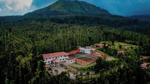 An aerial view of a resort with a large building surrounded by dense forest and a mountain in the background. - Anvitha Mansions (Chikkamagaluru)