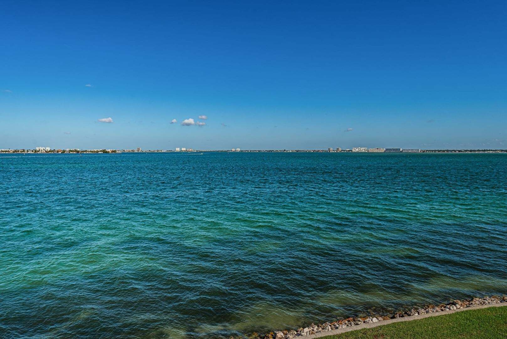 A clear view of a waterfront with calm water and a distant cityscape.