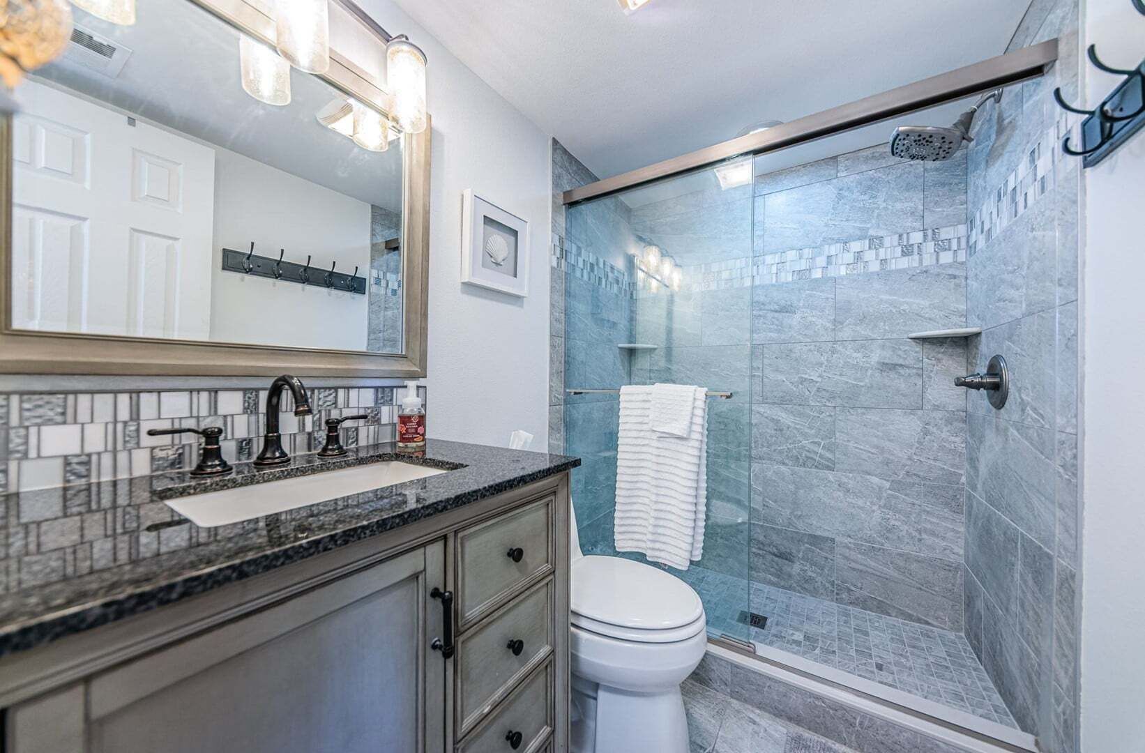 A bathroom with a glass-enclosed shower, a white toilet, and a vanity with a sink and mirror.