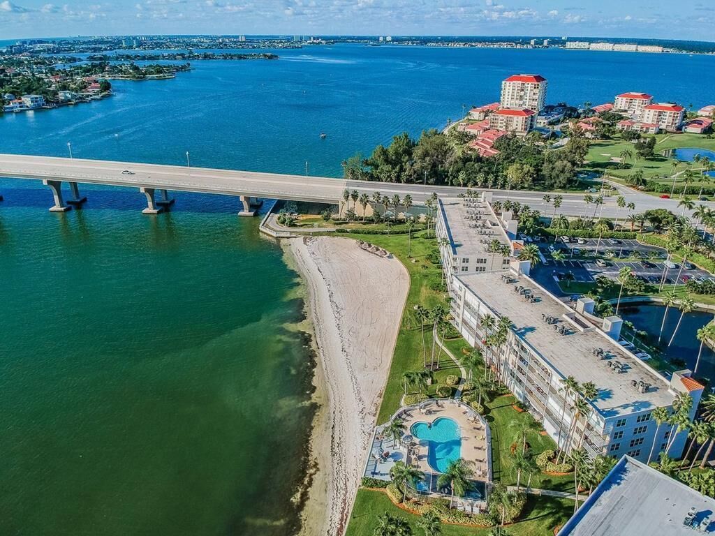 Vista aérea de una zona costera con un puente, una playa y un hotel con piscina y aparcamiento.