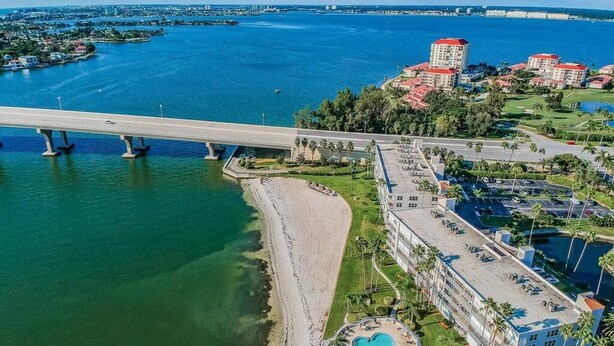 Vista aérea de una zona costera con un puente, una playa y un hotel con piscina y aparcamiento.