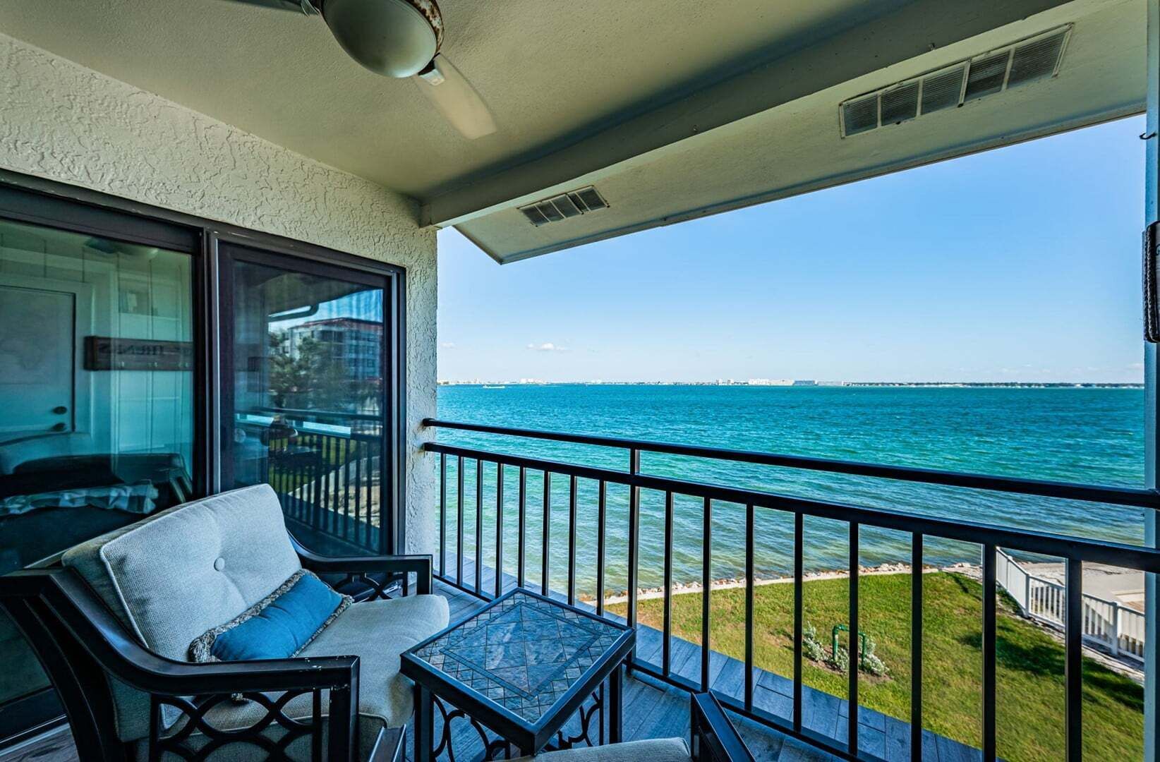 Ein Balkon mit Meerblick, ein Stuhl, ein kleiner Tisch und eine Glastür zu einem Innenraum.