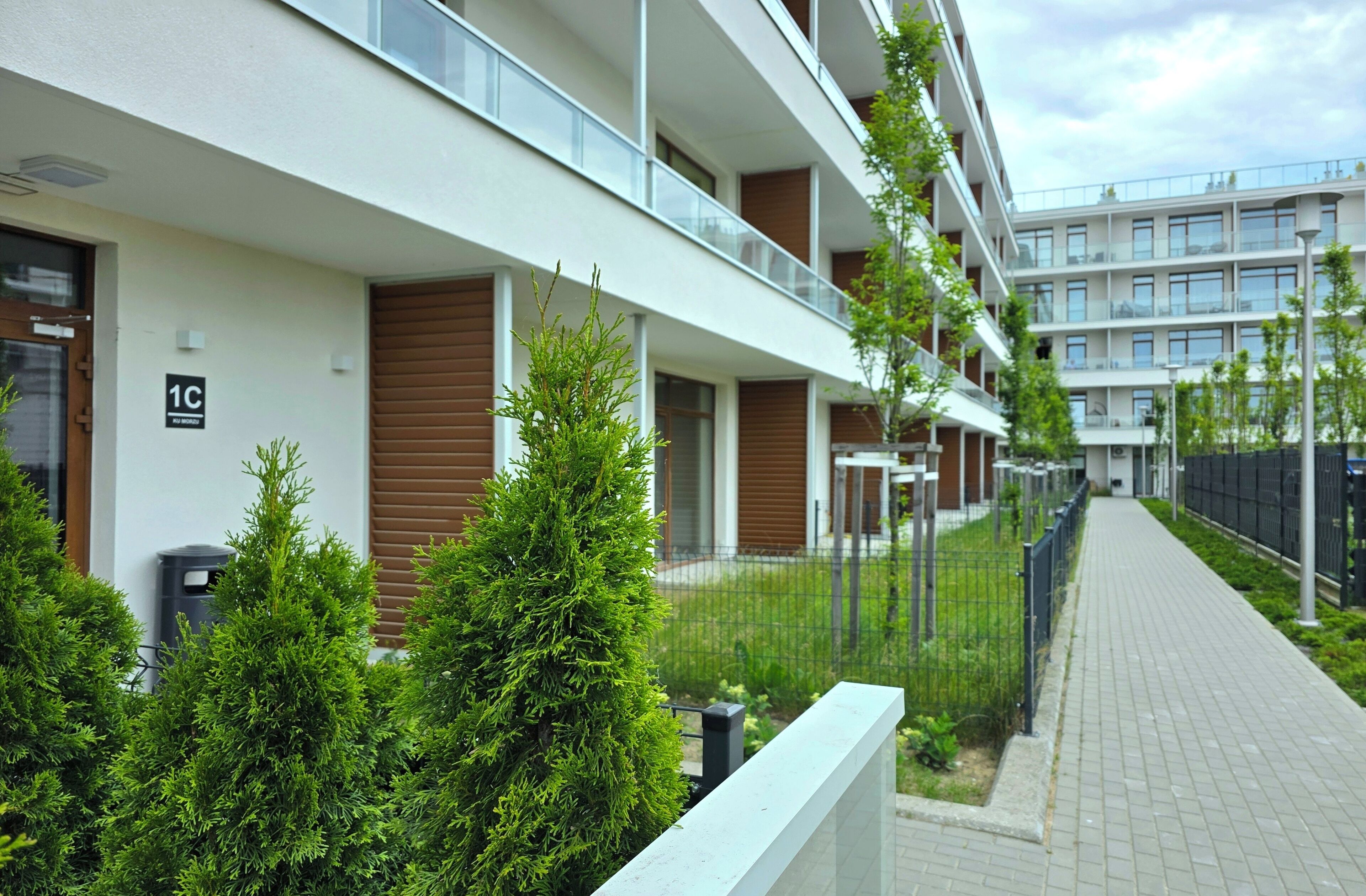 A modern apartment building with balconies, a paved walkway, and greenery.