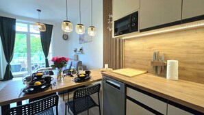 A modern kitchen with a wooden countertop, a dishwasher, and a microwave. There is a dining table with chairs and a vase of flowers. - Apartament Ku Morzu 27 - 365PAM (Sianożęty)