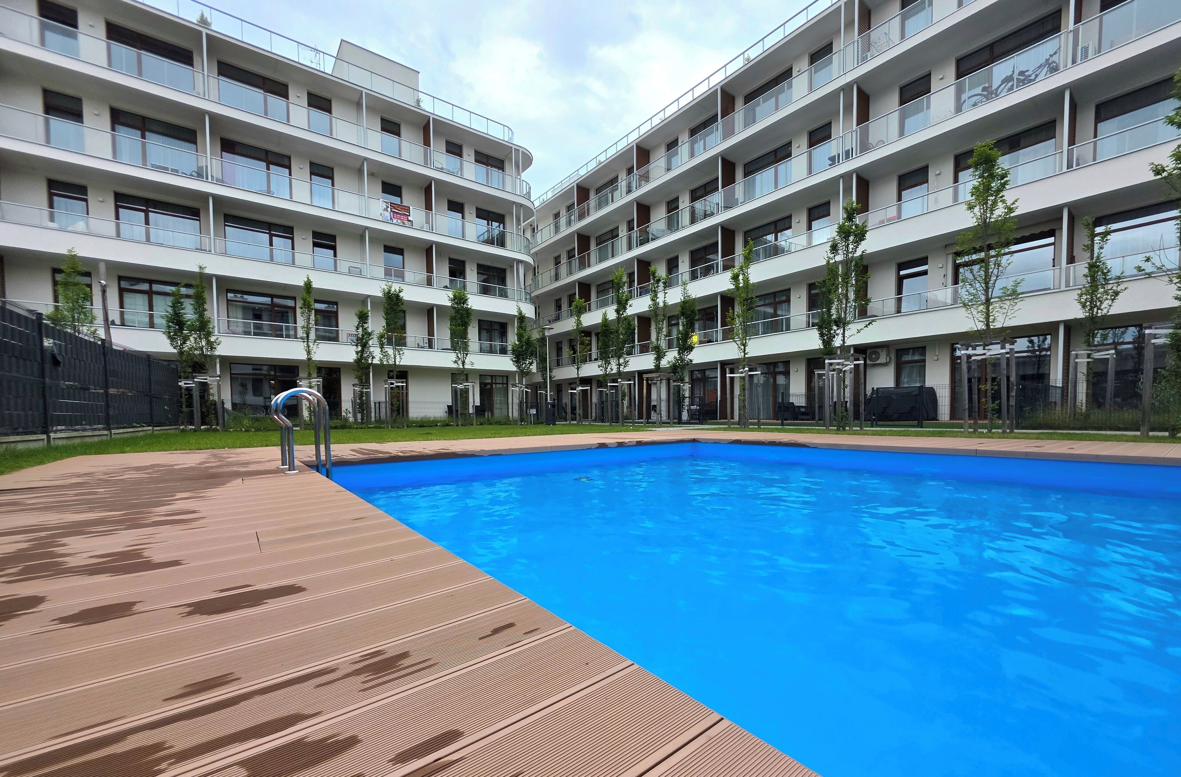 Un edificio moderno con piscina, varios balcones y una terraza de madera.