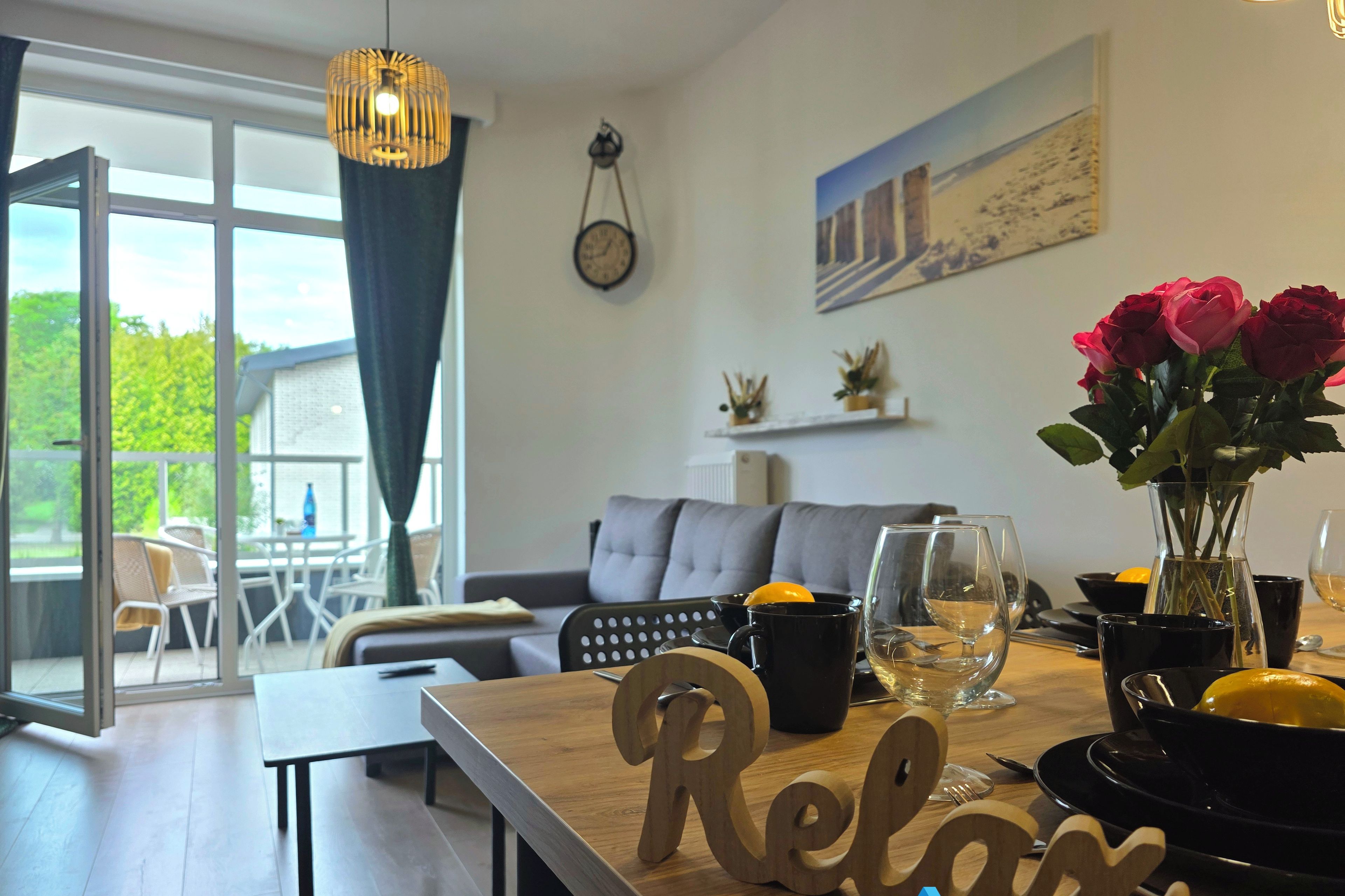 Un salon moderne avec une table en bois, un canapé et un coin repas. Une fenêtre offre une vue sur la verdure à l’extérieur.