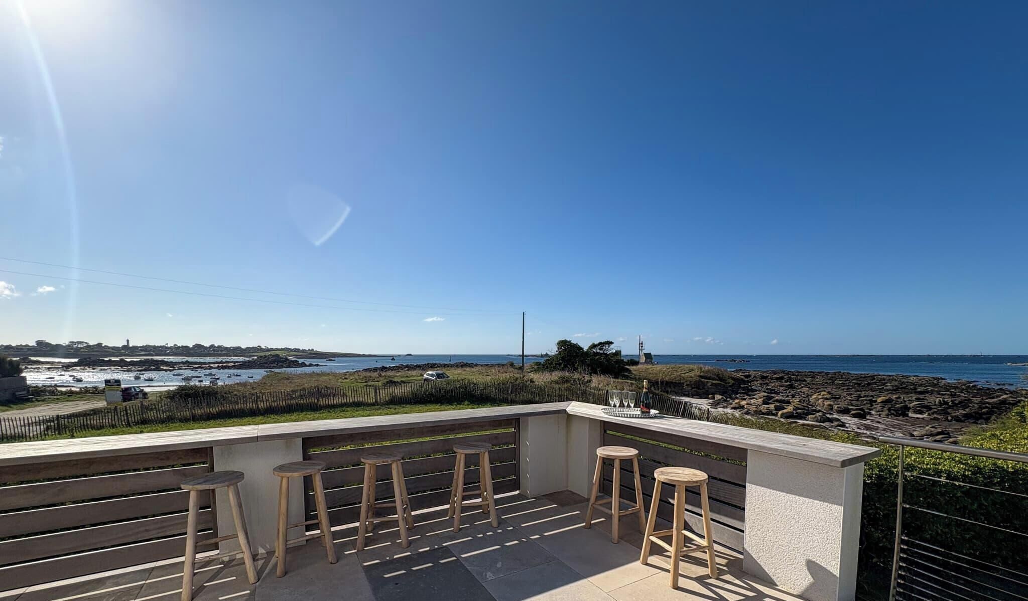 A balcony with wooden stools and a view of the sea.