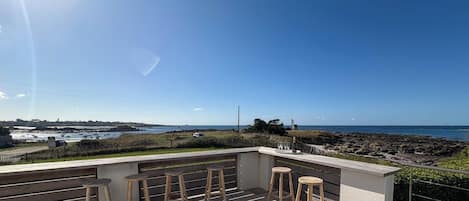 Un balcón con taburetes de madera y vista al mar.