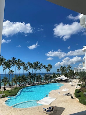 A resort pool area with a clear view of the ocean and palm trees, surrounded by resort buildings.