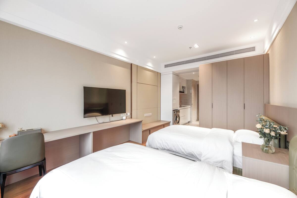 A modern hotel room with a large bed, a desk with a flat-screen TV, a chair, and a small bathroom area.