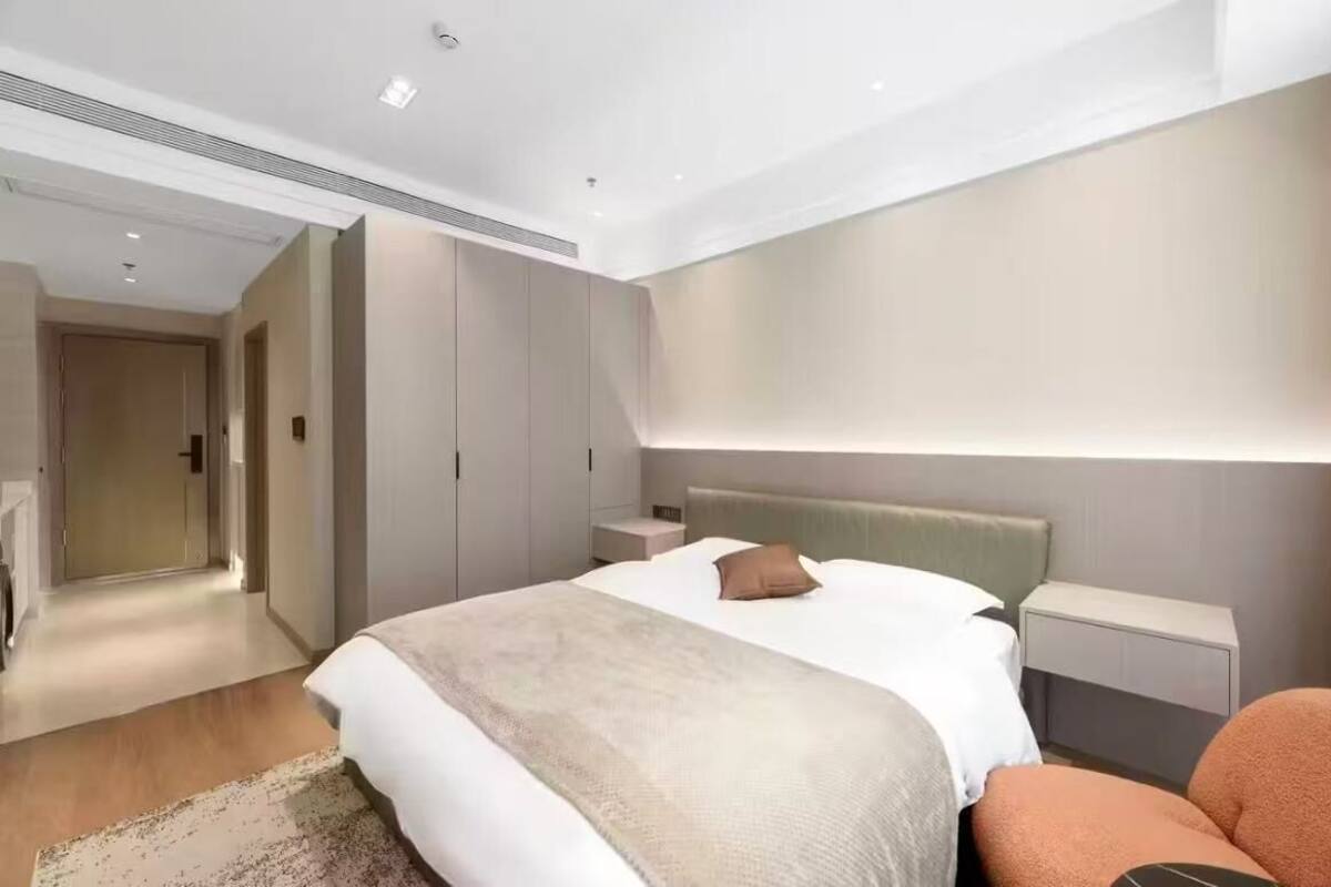 A modern hotel room with a large bed, bedside tables, a nightstand, and a walk-in closet.