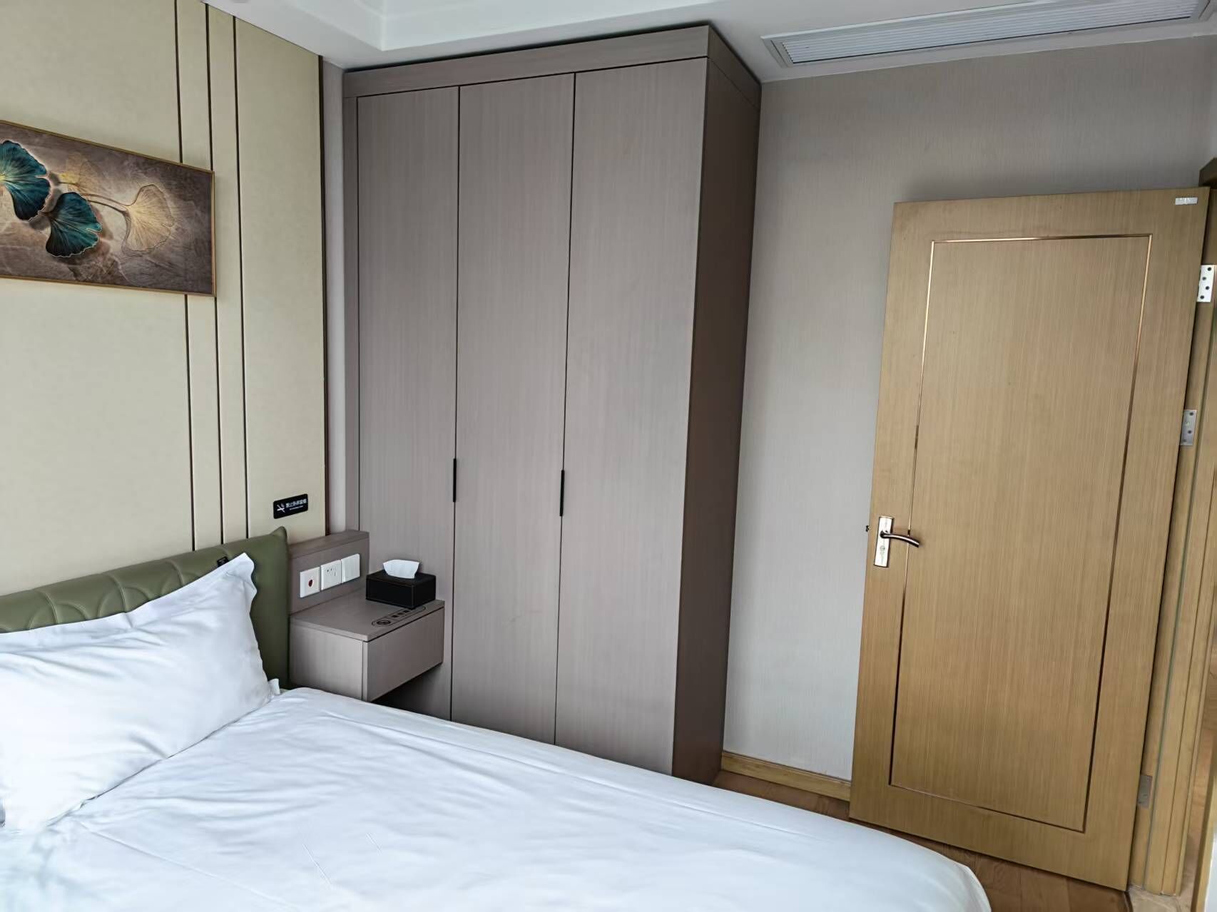 Habitación de hotel con cama, armario, mesita de noche con caja de pañuelos y puerta de madera.