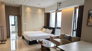 Moderni hotellihuone, jossa on sänky, sohva, ruokapöytä ja roskakori.
