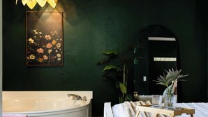 Ein modernes Badezimmer mit einer freistehenden Badewanne, einem großen Spiegel und einem Nachttisch mit Gläsern.