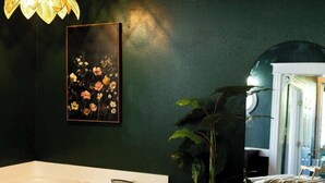 Ein Schlafzimmer mit einem großen Bett, einem Nachttisch, einer Hängeleuchte, einem gerahmten Blumenbild und einem großen Fenster.