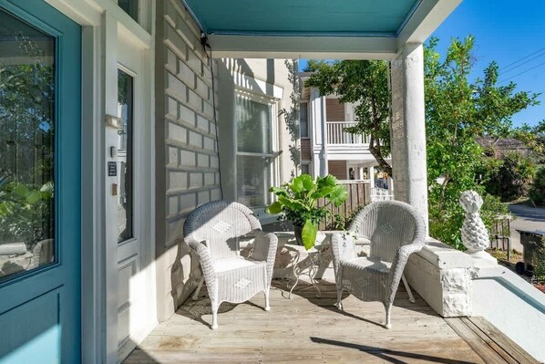 A covered porch with wicker furniture and a potted plant.