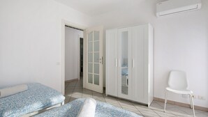 A bedroom with two beds, a wardrobe, a chair, and an air conditioning unit. - Casa Vacanze “Martina” with Private Terrace near Lake Como (San Fermo della Battaglia)