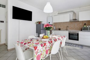 Une cuisine moderne avec des meubles blancs, un pare-feu en carrelage, une table à manger recouverte d’une nappe à motifs floraux et des chaises blanches.