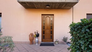 A building entrance with a wooden door, a tiled patio, a potted plant, and a large vase. - Casa Vacanze “Martina” with Private Terrace near Lake Como (San Fermo della Battaglia)