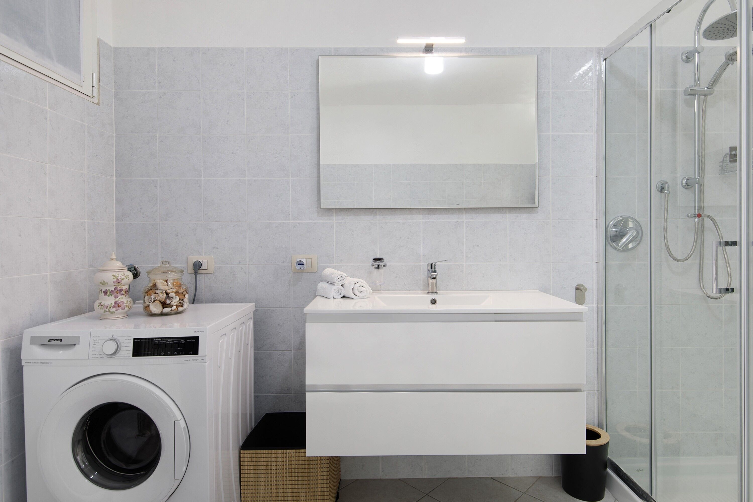 Ein modernes Badezimmer mit Waschmaschine, Waschbecken und einer Duschkabine aus Glas.