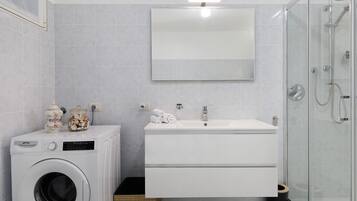Ein modernes Badezimmer mit Waschmaschine, Waschbecken und einer Duschkabine aus Glas.