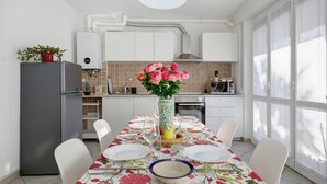 A modern kitchen with white cabinets, a grey refrigerator, a dining table with a floral tablecloth, and a vase with flowers. - Casa Vacanze “Martina” with Private Terrace near Lake Como (San Fermo della Battaglia)