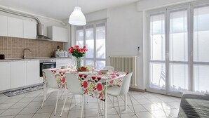 A modern kitchen with white cabinets, a dining table with a floral tablecloth, and a large window with a view. - Casa Vacanze “Martina” with Private Terrace near Lake Como (San Fermo della Battaglia)