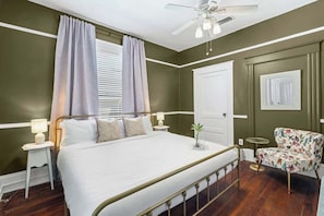 Un dormitorio con cama, mesitas de noche, una silla, ventilador de techo y una puerta.
