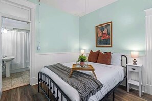 Ein Schlafzimmer mit Bett, Nachttischen, einem Gemälde und einem Badezimmer mit Waschbecken und Dusche.