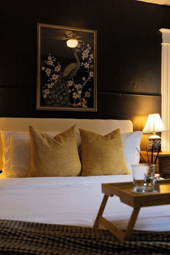 A hotel room with a bed, pillows, a nightstand, a lamp, and a framed artwork on the wall.