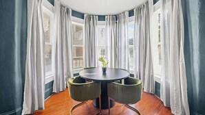 A round table with two chairs, a potted plant, and a view through large windows with curtains. - Crystal Room | Team Joseph Ellen (St. Augustine)