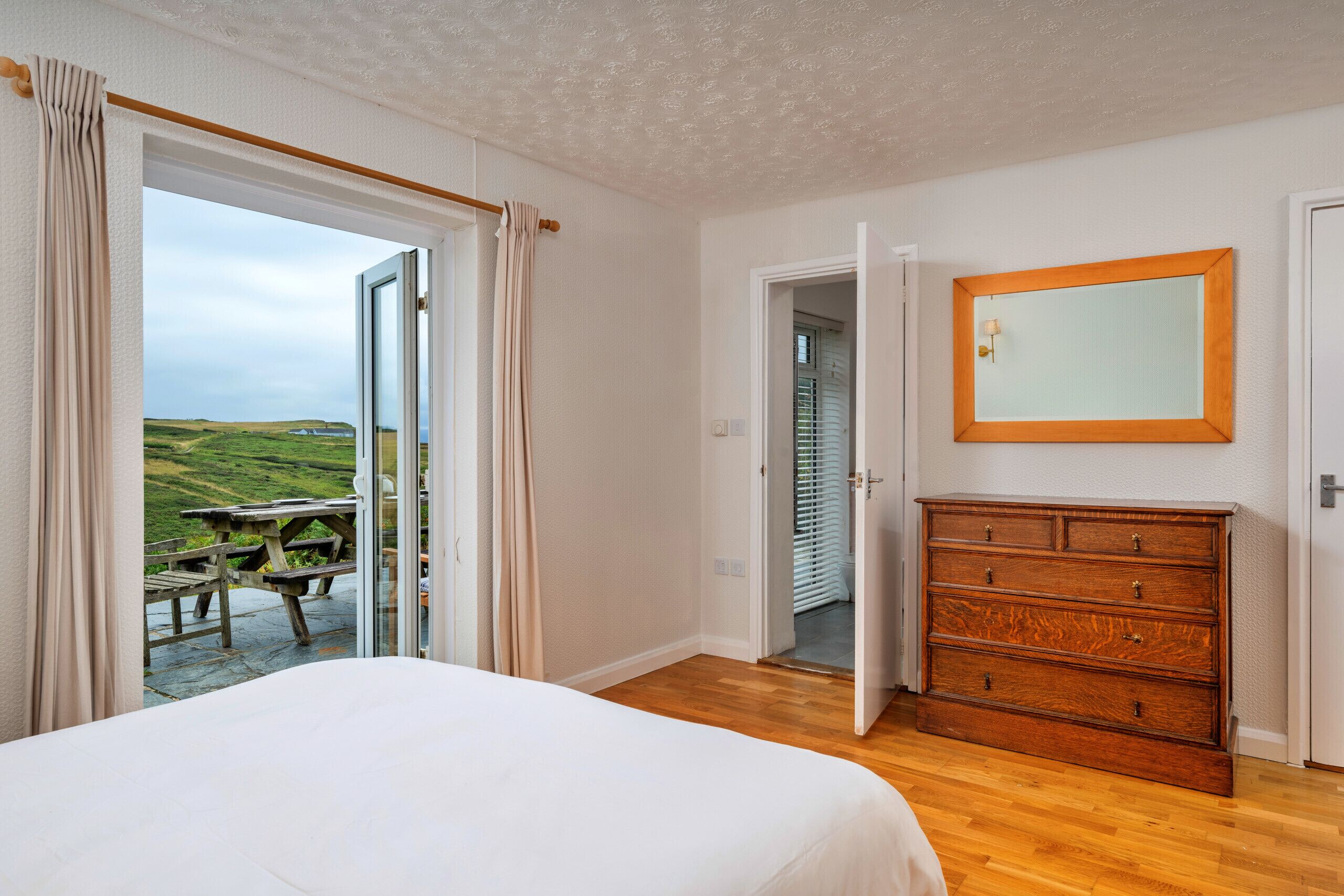 Una camera da letto con un letto grande, una cassettiera in legno e vista su un paesaggio suggestivo attraverso una porta aperta.