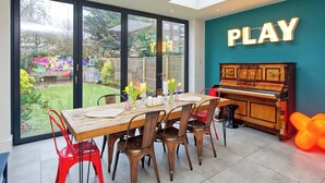Zona pranzo con un pianoforte, un cartello con scritto 'PLAY' e vista sul giardino.