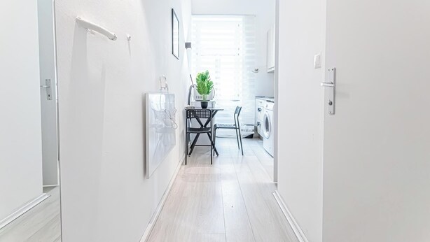 A narrow hallway with a dining area at the end, featuring a table and chairs, a potted plant, and a washing machine. - Comfy Apt Long Stay Near Praterstern (Vienna)