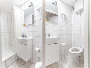 A modern bathroom with white tiles, a sink, a toilet, and a shower area.