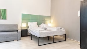 A modern bedroom with a bed, a grey sofa, a nightstand, and a wall-mounted lamp. - Comfy Apt Long Stay Near Praterstern (Vienna)