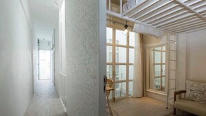A spacious hallway with a high ceiling and large windows. There is a wooden chair and a sofa in the room. - TWH Hostel Bangkok (Bangkok)