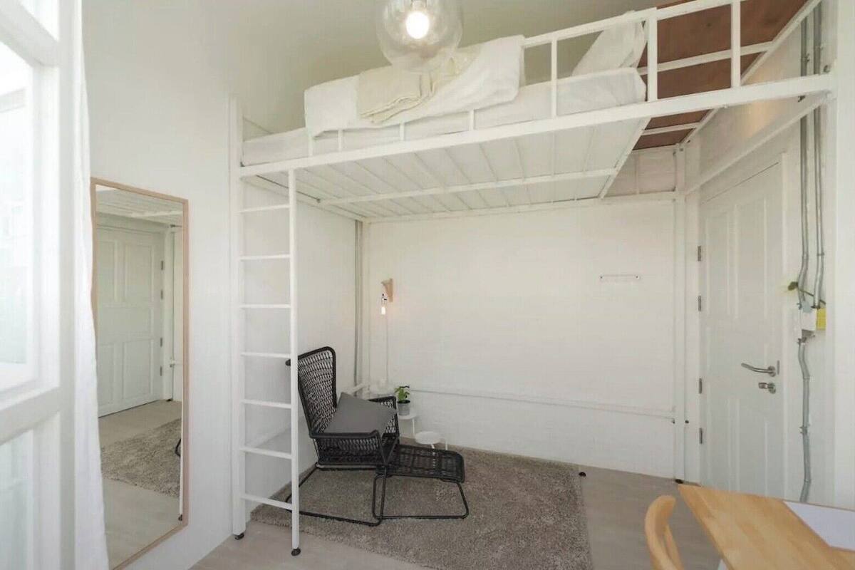 A compact room with a bunk bed, a small desk with a chair, a mirror, and a door.