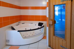 Et badeværelse med et hvidt badekar, orange fliser og en trædør med et glasvindue.
