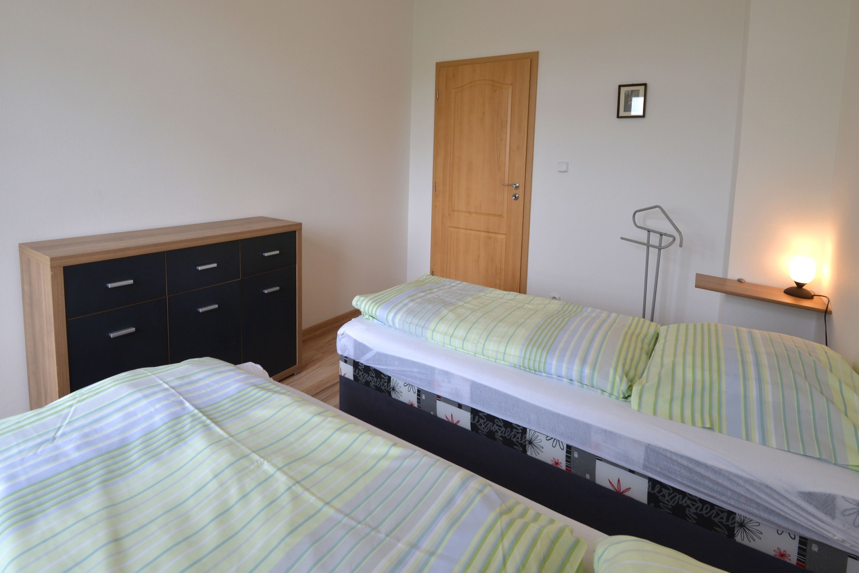 Une chambre avec deux lits, une armoire, une porte et une table de chevet avec une lampe.