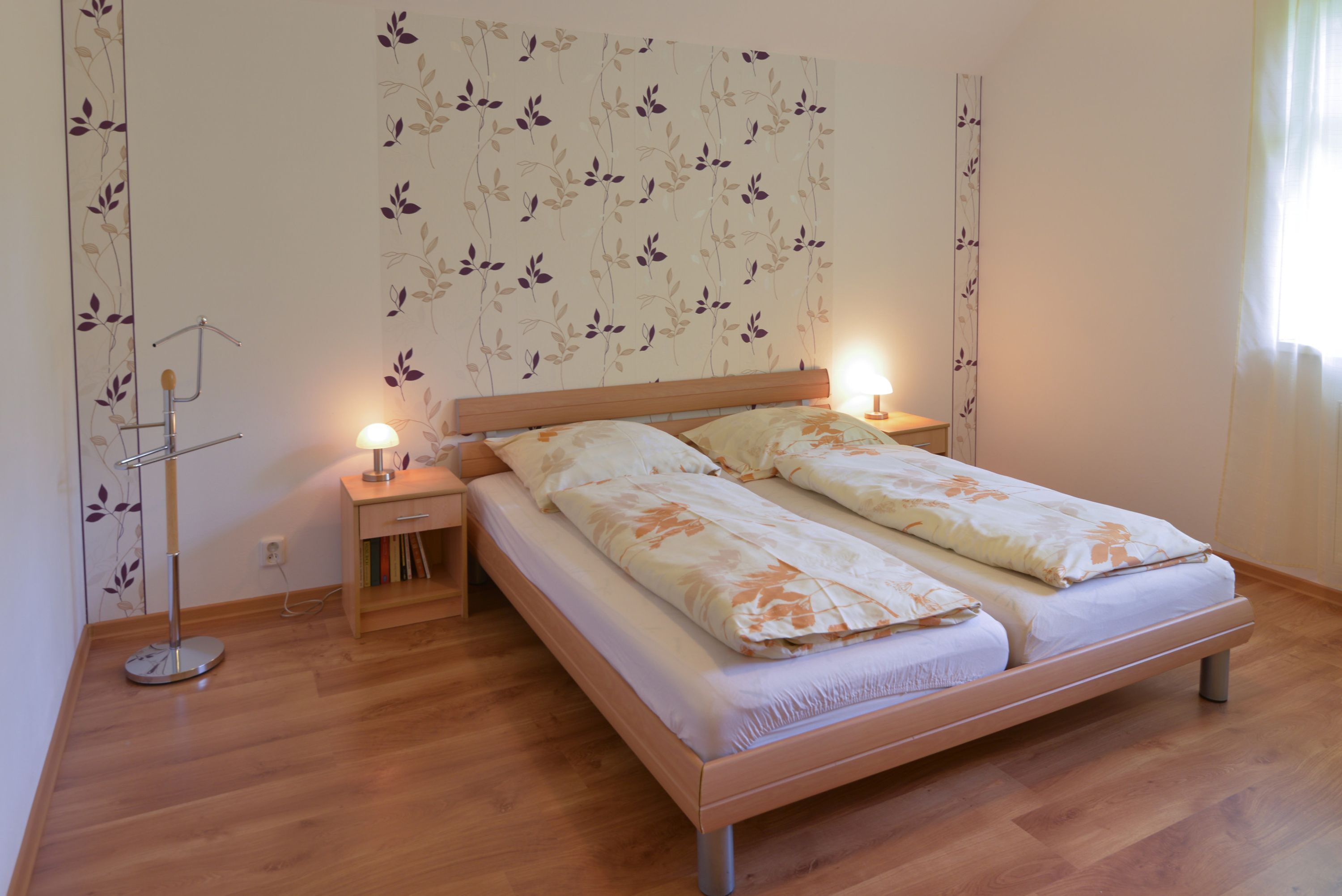 A bedroom with a wooden bed, two bedside lamps, a nightstand, and a wall-mounted radiator.