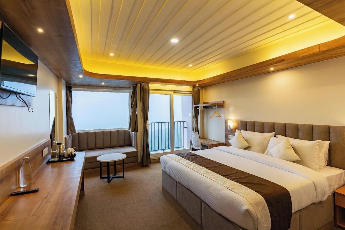 A hotel room with a large bed, a small round table, a sofa, and a balcony with a view.