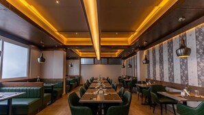 Ein Restaurant mit langen Gemeinschaftstischen, grün gepolsterten Sitzbänken und Pendelleuchten.
