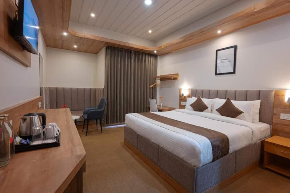 A hotel room with a large bed, a desk with a coffee maker, a chair, and a TV mounted on the wall.