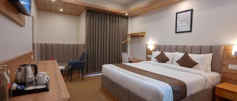 Habitación de hotel con una cama grande, un escritorio con cafetera, una silla y un televisor montado en la pared.