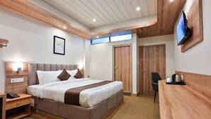 Ein modernes Hotelzimmer mit einem großen Bett, einem Holzkopfteil, einem Nachttisch mit Telefon, einem Schreibtisch mit Wasserkocher und einem an der Wand befestigten Fernseher.