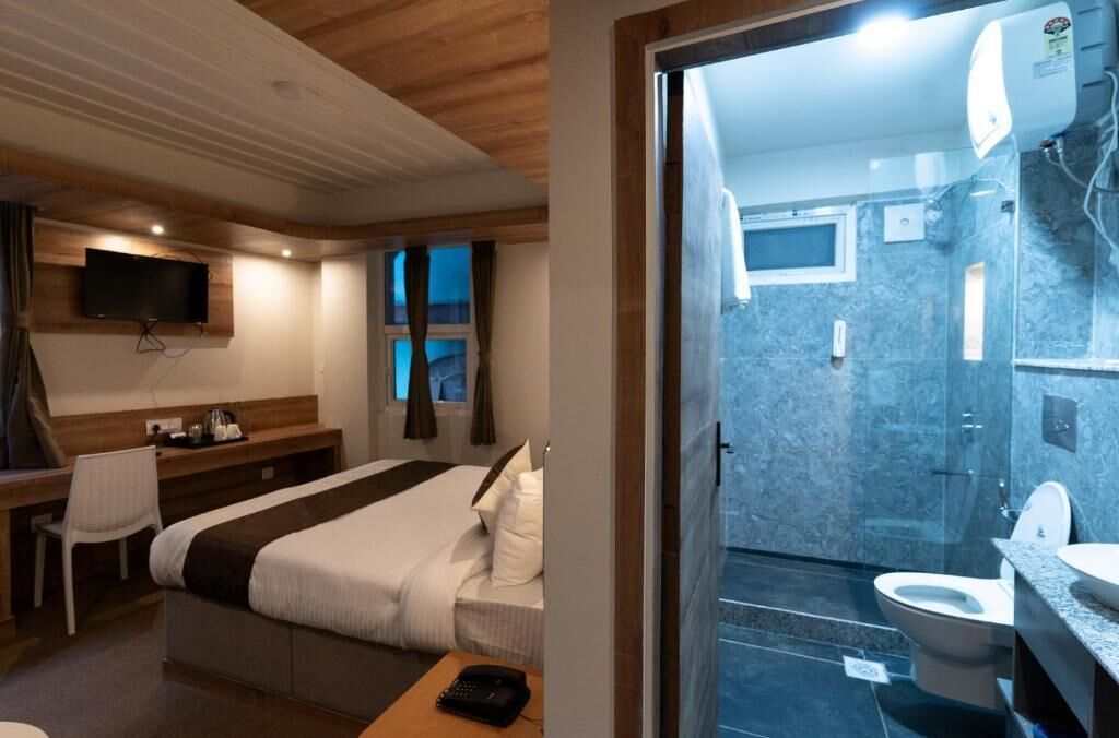 A hotel room with a bed, desk, chair, TV, and a bathroom with a shower, toilet, and sink.