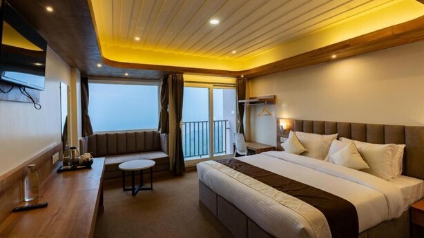 Ein Hotelzimmer mit einem großen Bett, einer kleinen Sitzecke, einem Schreibtisch und Blick ins Freie.