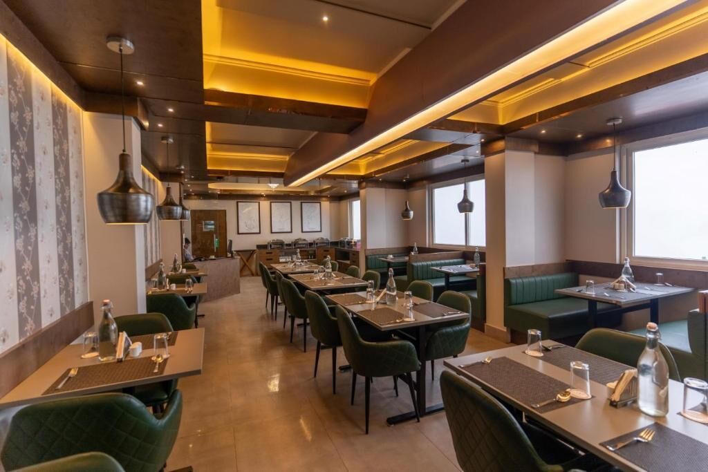 A restaurant with multiple tables and booths, featuring a modern design with green upholstered seating and pendant lighting.