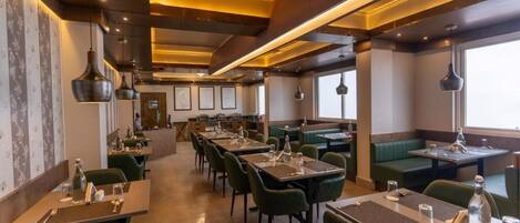 A restaurant with multiple tables and booths, featuring a modern design with green upholstered seating and pendant lighting.
